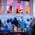 Eine sommerliche Musikveranstaltung mit Liveband in einem Pavillon am Meer zieht begeisterte Zuschauer an.A summer music event with a live band in a pavilion by the sea attracts an enthusiastic audience.