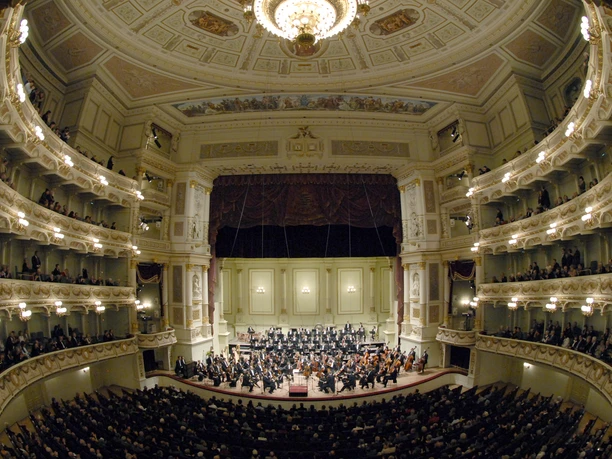 Innenansicht der prachtvollen Semperoper in Dresden mit beleuchtetem Kronleuchter und Orchester.