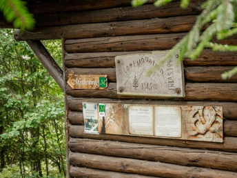 Historische Schutzhütte aus Holz an der Herlingsburg, umgeben von dichtem Wald, mit Informationstafeln.