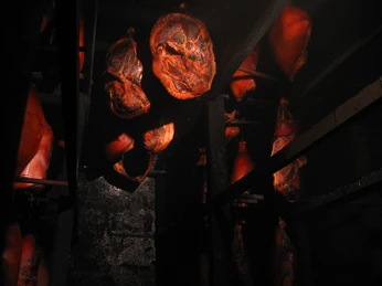 Schinken im Rauch Verschiedene Schinken hängen dicht beieinander im dunklen Raum, umgeben von mystischem Rauch.