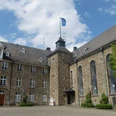 Schloss Hückeswagen Historisches Schloss-Ensemble mit Bruchsteinmauern, zentralem Turm und Flügeln unter blauem Himmel.