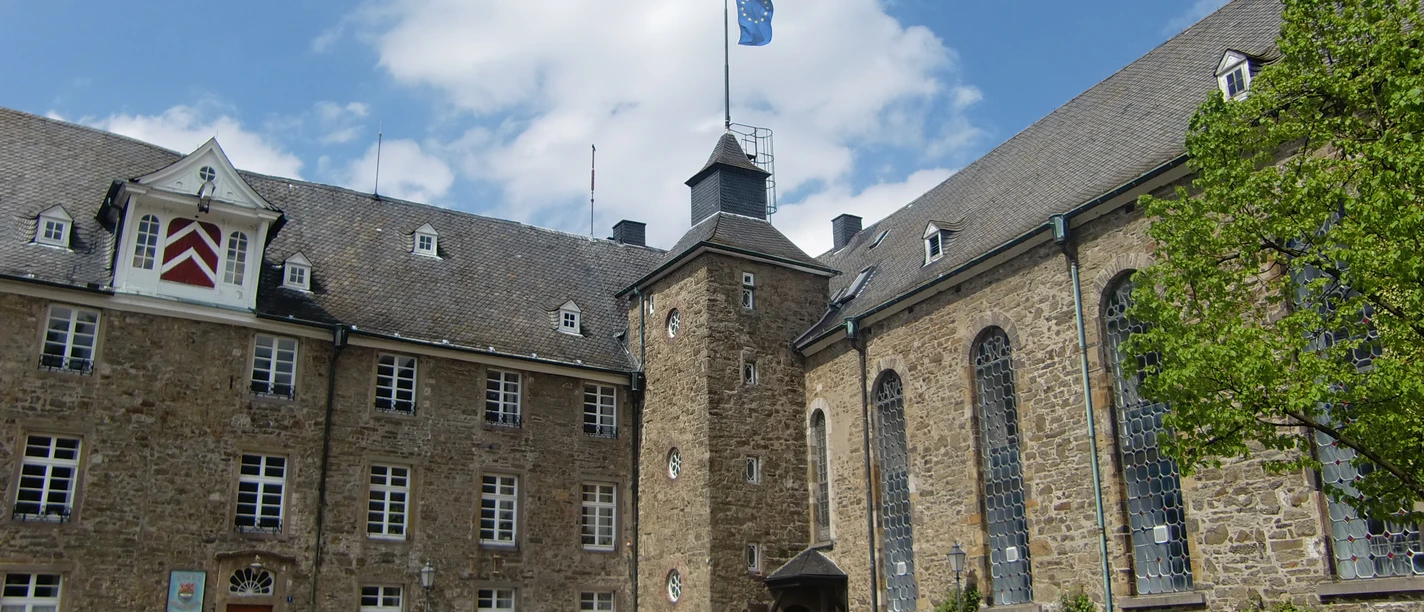 Schloss Hückeswagen Historisches Schloss-Ensemble mit Bruchsteinmauern, zentralem Turm und Flügeln unter blauem Himmel.