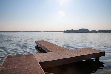 steg-dlrg-zwischenahner-meer.jpg Een steiger steekt uit in het Zwischenahner Meer, omgeven door kalm water en een verre kust op de achtergrond.