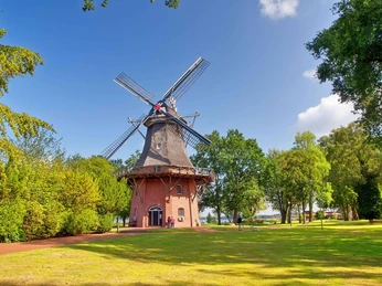 muehle-kurpark-freilichtmuseum-sommer.jpg Historische Windmühle im Kurpark, umgeben von grünen Bäumen unter blauem Sommerhimmel.Historic windmill in the spa gardens, surrounded by green trees under a blue summer sky.Historisk vindmølle i spa-haven, omgivet af grønne træer under en blå sommerhimmel.Historische windmolen in de tuinen van het kuuroord, omringd door groene bomen onder een blauwe zomerhemel.