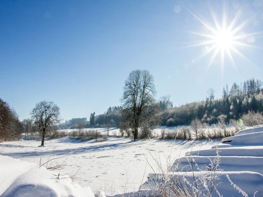 Verschneite Landschaft im Meintetal, klare Sicht auf Bäume und Hügel unter strahlendem Sonnenschein.
