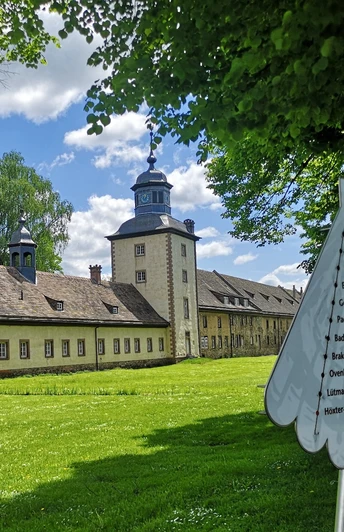 Weltkulturerbe Schloss Corvey mit parkähnlicher Anlage, von Pilgerwegweiser im Vordergrund ergänzt.