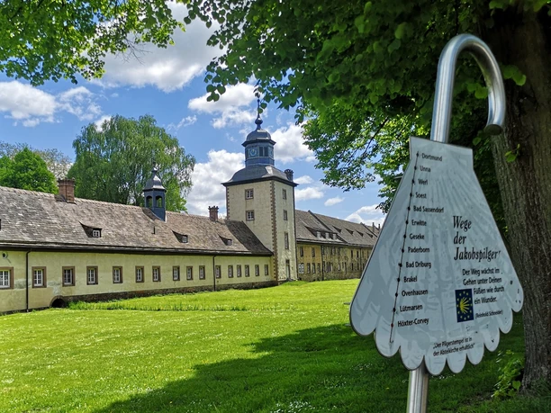Corvey als Pilgerziel Weltkulturerbe Schloss Corvey mit parkähnlicher Anlage, von Pilgerwegweiser im Vordergrund ergänzt.