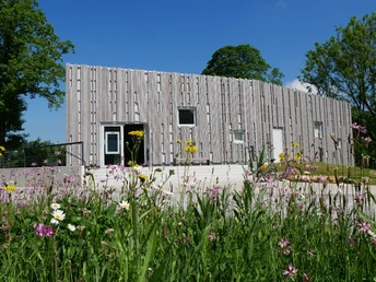 Besucherzentrum Fourm Abtei (Marienmünster) Das Besucherzentrum besteht aus einem modernen, hölzernen Gebäude, umgeben von bunten Wildblumen.