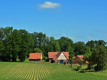 TERRA.track Kettelsberg Drei Backsteinhäuser mit roten Dächern vor einem Feld und üppigem Baumbestand.