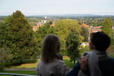 Twee mensen genieten van het uitzicht op een groen parklandschap met een kerktoren in de verte.
