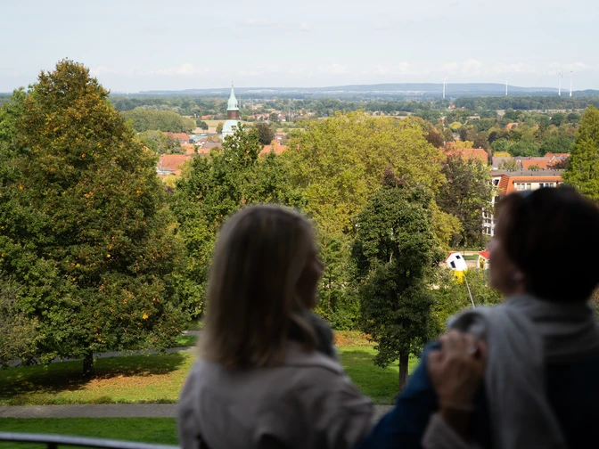 Zwei Personen genießen die Aussicht auf eine grüne Parklandschaft mit Kirchturm in der Ferne.
