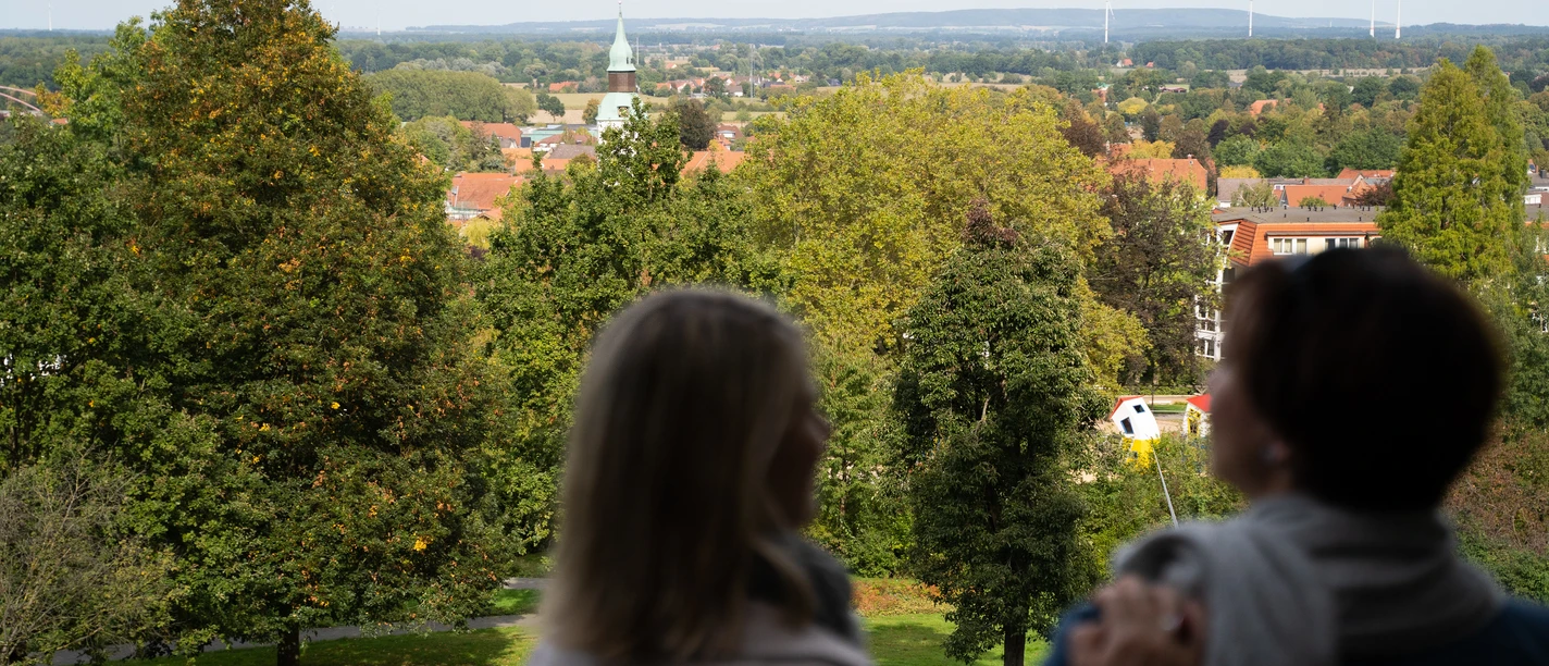 Blick von der Himmelsterrasse Zwei Personen genießen die Aussicht auf eine grüne Parklandschaft mit Kirchturm in der Ferne.