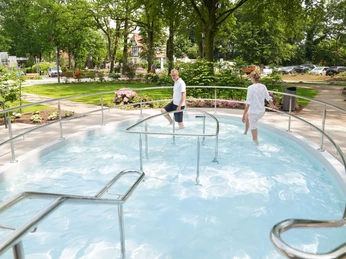 Kneippbecken-Bad-Zwischenahn-Wassertreten Foto von zwei Personen im barrierefreien Kneippbecken in einer grünen Parklandschaft mit Bäumen.