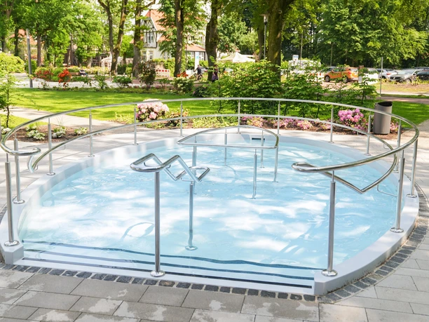 Kneippbecken-Bad-Zwischenahn-Sommer Sommerliches Kneippbecken im Park, umgeben von grünen Bäumen und Blumen, mit Edelstahlgeländern.