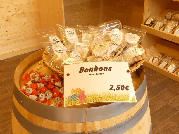 Hofladen Garrelts Aurich Bonbons Ein Holzfass im Hofladen präsentiert verpackte Bonbons mit Preisschild neben Gemüsekisten.