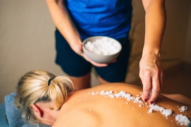 Wellness Eine Frau genießt eine Salzbehandlung auf dem Rücken im Wellnessbereich.