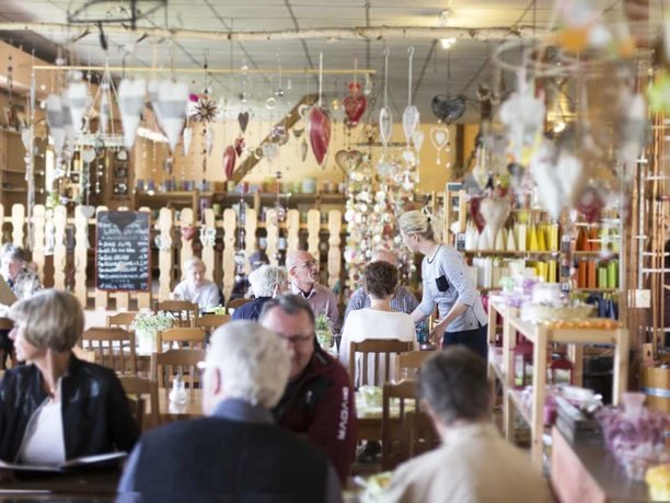 A cozy café with wooden furniture, decorative hearts and candles; guests sit at tables while a waitress takes orders.