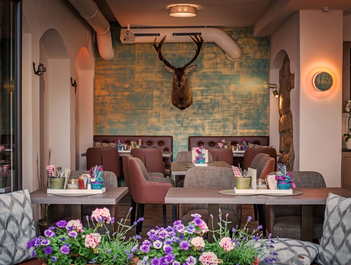 Restaurace Platzhirsch v Pirně Gemütliches Café mit braunen Sesseln, blumengeschmückten Tischen und einem Hirschkopf an der türkis-gelben Wand, im Vordergrund bunte Blumen.Cosy café with brown armchairs, flower-decorated tables and a stag's head on the turquoise-yellow wall, with colorful flowers in the foreground.Útulná kavárna s hnědými křesly, květinami zdobenými stolky a jelení hlavou na tyrkysově žluté stěně s barevnými květinami v popředí.Przytulna kawiarnia z brązowymi fotelami, stolikami ozdobionymi kwiatami i głową jelenia na turkusowo-żółtej ścianie, z kolorowymi kwiatami na pierwszym planie.Gezellig café met bruine fauteuils, met bloemen versierde tafels en een hertenkop op de turkoois-gele muur, met kleurrijke bloemen op de voorgrond.Accogliente caffè con poltrone marroni, tavoli decorati con fiori e una testa di cervo sulla parete giallo turchese, con fiori colorati in primo piano.