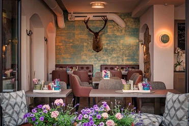 Restaurant Platzhirsch in Pirna Gemütliches Café mit braunen Sesseln, blumengeschmückten Tischen und einem Hirschkopf an der türkis-gelben Wand, im Vordergrund bunte Blumen.