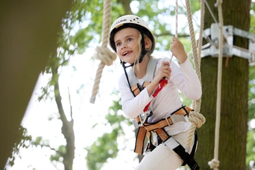 Fröhliches Mädchen klettert im Hochseilgarten.