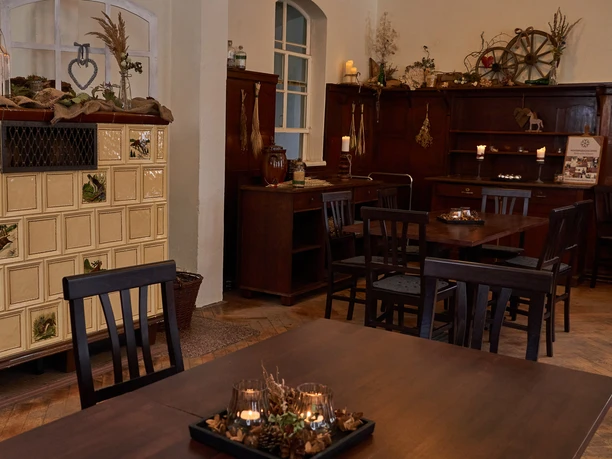 Cozy café with wooden furniture and large windows offering a view of a snowy landscape; warm lighting and decorative plants.