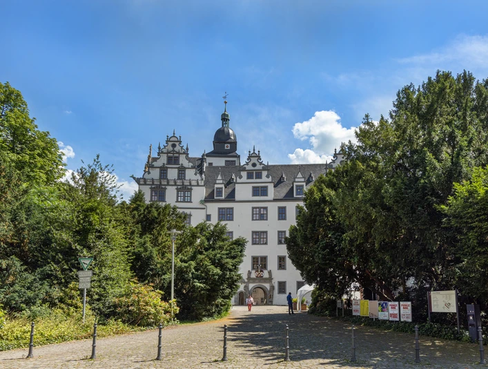 Renaissance-Schloss mit weißer Fassade und Türmen, umgeben von Bäumen unter blauem Himmel.
