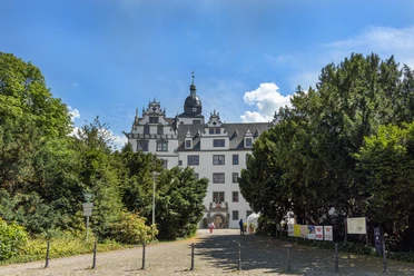 Schloss Wolfsburg Außenansicht Renaissance-Schloss mit weißer Fassade und Türmen, umgeben von Bäumen unter blauem Himmel.