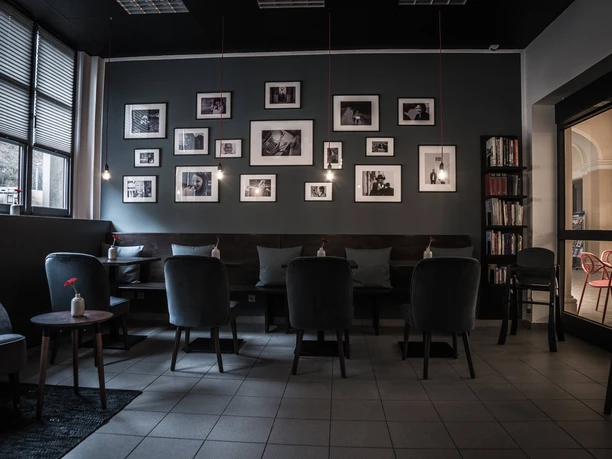 Cozy café with gray chairs, wooden tables and black and white photos on the wall; subdued lighting and a quiet atmosphere.