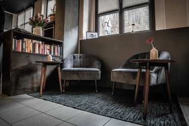 drehscheibe Gemütliche Sitzecke mit zwei grauen Sesseln, einem Holztisch mit roter Blume in Vase, Bücherregal und Fenster im Hintergrund.