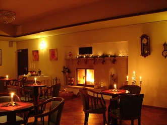 Gezellig café met open haard, kaarsen op tafels, warm licht en kerstversieringen creëren een uitnodigende sfeer.