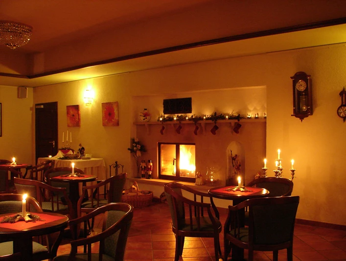 Gemütliches Café mit Kaminfeuer, Kerzen auf Tischen, warmem Licht und weihnachtlicher Dekoration, schafft eine einladende Atmosphäre.A cozy café with an open fire, candles on tables, warm lighting and Christmas decorations creates an inviting atmosphere.Útulná kavárna s otevřeným ohněm, svíčkami na stolech, teplým světlem a vánoční výzdobou vytváří příjemnou atmosféru.Przytulna kawiarnia z otwartym ogniem, świecami na stołach, ciepłym światłem i świątecznymi dekoracjami tworzy zachęcającą atmosferę.Gezellig café met open haard, kaarsen op tafels, warm licht en kerstversieringen creëren een uitnodigende sfeer.Accogliente caffetteria con camino, candele sui tavoli, luce calda e decorazioni natalizie creano un'atmosfera invitante.