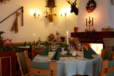 Cozy restaurant with table setting, green napkins, candlelight and open fire; rustic decoration with antlers and flowers.
