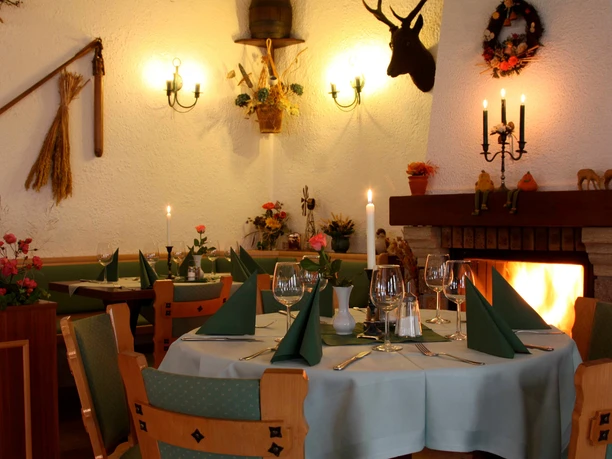 Cozy restaurant with table setting, green napkins, candlelight and open fire; rustic decoration with antlers and flowers.