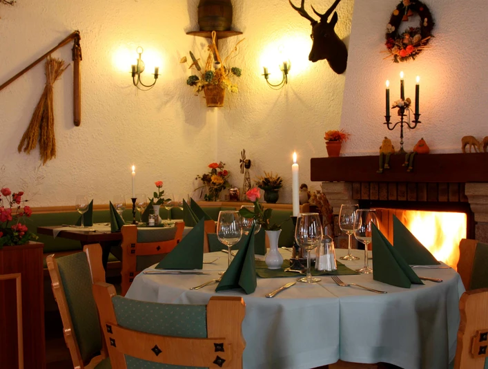 Gasthof Hertigswalde Gastraum Gemütliches Restaurant mit gedecktem Tisch, grünen Servietten, Kerzenlicht und Kaminfeuer; rustikale Dekoration mit Geweih und Blumen.Cozy restaurant with table setting, green napkins, candlelight and open fire; rustic decoration with antlers and flowers.Útulná restaurace s prostřeným stolem, zelenými ubrousky, světlem svíček a otevřeným ohněm; rustikální výzdoba s parožím a květinami.Przytulna restauracja z nakrytym stołem, zielonymi serwetkami, świecami i otwartym ogniem; rustykalny wystrój z porożami i kwiatami.Gezellig restaurant met gedekte tafel, groene servetten, kaarslicht en open haard; rustieke decoratie met geweien en bloemen.Ristorante accogliente con tavolo apparecchiato, tovaglioli verdi, lume di candela e fuoco aperto; decorazione rustica con corna e fiori.