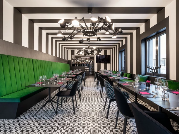 Modern restaurant with black and white striped walls, green benches and elegant table decorations, including glasses and pink napkins.
