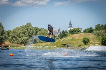 WakePark mit dem Schloss Wolfsburg im Hintergrund Wakeboardfahrer springt über Wasser, im Hintergrund Schloss Wolfsburg.