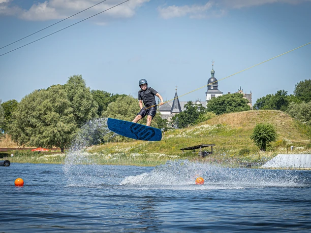 WakePark mit dem Schloss Wolfsburg im Hintergrund Wakeboardfahrer springt über Wasser, im Hintergrund Schloss Wolfsburg.