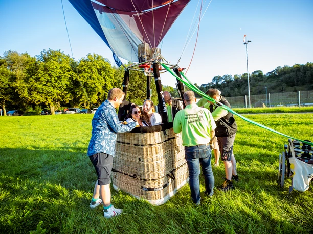 Start im barrierefreien Korb Eine Gruppe von Menschen bereitet sich auf eine Heißluftballonfahrt in einem grünen Feld vor.