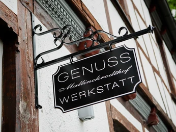 Schmiedeeisernes Schild einer Fachwerkhausfassade mit Aufschrift "Genuss Werkstatt Mallinckrodtshof".