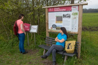 TERRA.track Eiszeit-Entdeckerpfad Two women explore an educational trail with information boards about the Ice Age in a rural setting.