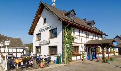 Sinsperter Hof Ein Fachwerkhaus mit Restaurant und Terrasse voller Pflanzen unter klarem, blauem Himmel.