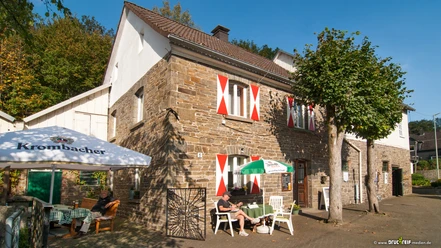 Mühlencafé Nespen Historisches Fachwerkhaus mit rot-weißen Fensterläden, umgeben von Bäumen und Sonnenschirmen.