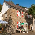 Mühlencafé Nespen Historisches Fachwerkhaus mit rot-weißen Fensterläden, umgeben von Bäumen und Sonnenschirmen.