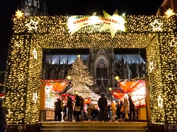 Weihnachtsmarkt am Kölner Dom Ein festlich beleuchtetes Eingangstor mit einem großen Weihnachtsbaum führt zum lebhaften Weihnachtsmarkt vor dem majestätischen Kölner Dom.A festively illuminated entrance gate with a large Christmas tree leads to the lively Christmas market in front of the majestic Cologne Cathedral.