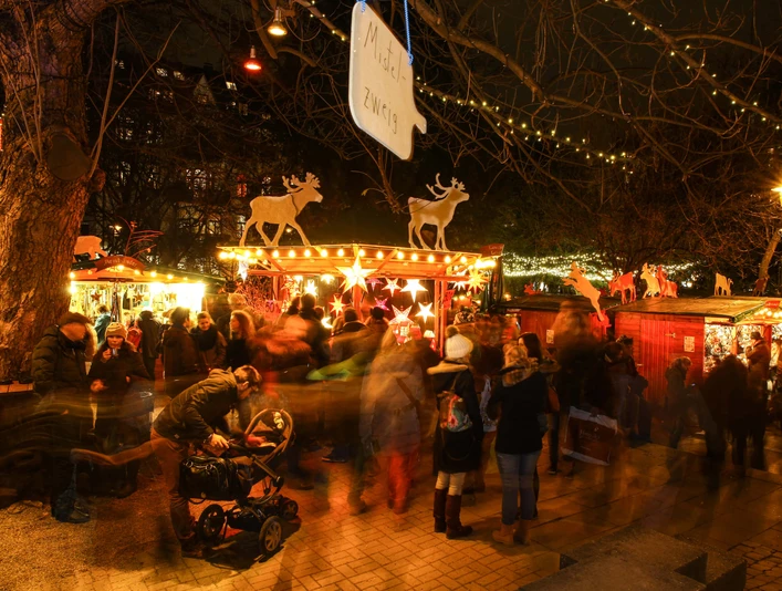Weihnachtsmarkt im Stadtgarten Ein belebter Weihnachtsmarkt im Stadtgarten Köln bei Nacht, mit leuchtenden Ständen und Menschen.A lively Christmas market in Cologne's Stadtgarten at night, with illuminated stalls and people.