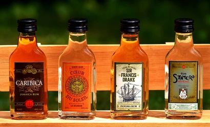 rum_flaschen Vier kleine Rumflaschen stehen nebeneinander auf einer Holzbank. Jede Flasche trägt ein eigenes Etikett.