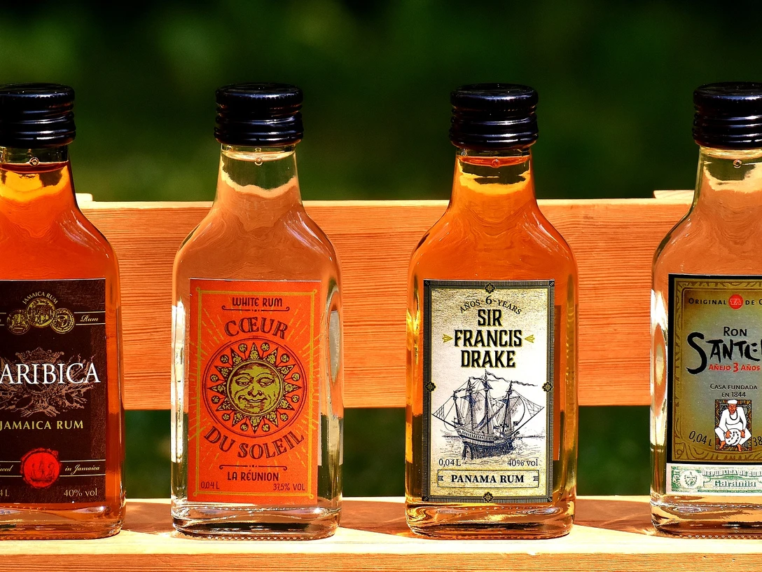 rum_flaschen Vier kleine Rumflaschen stehen nebeneinander auf einer Holzbank. Jede Flasche trägt ein eigenes Etikett.