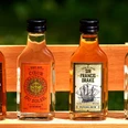 rum_flaschen Vier kleine Rumflaschen stehen nebeneinander auf einer Holzbank. Jede Flasche trägt ein eigenes Etikett.