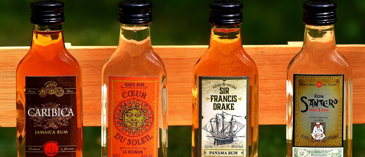 rum_flaschen Vier kleine Rumflaschen stehen nebeneinander auf einer Holzbank. Jede Flasche trägt ein eigenes Etikett.