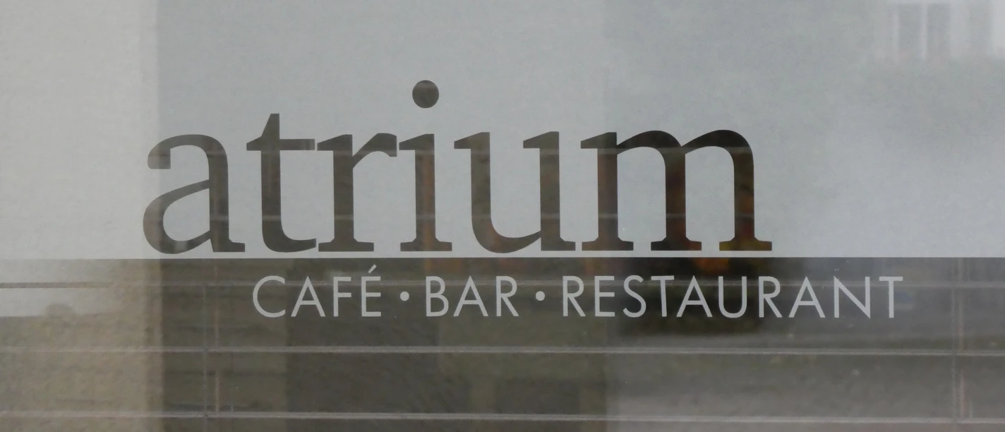 Lettering "Atrium Café Bar Restaurant" on a glass surface, behind it blurred building structures.
